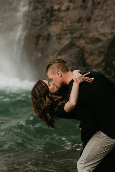 Couple kissing in front of waterfall in Alberta, engagement photo inspiration, featured on Bronte Bride.