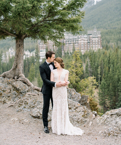 Sophisticated and timeless wedding inspiration, bride and groom embracing in Banff, Alberta with the Fairmont Springs Hotel in distance.