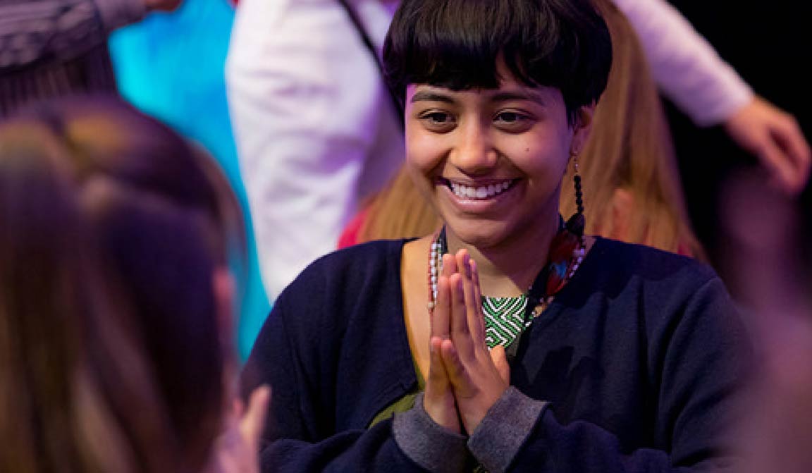 A smiling person, hands held together in a grateful gesture