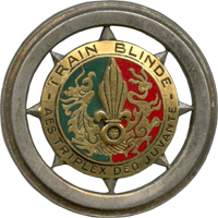 A circular insignia, divided roughly into green and red halves. The phrase "Train Blinde – Aes Triplex Deo Juvante" surrounds the coloured halves.