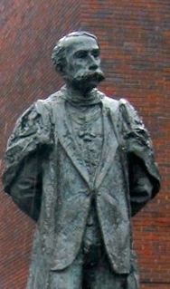 photograph of modern statue of Edwardian male figure with a large moustache in academic gown and wearing badge of the Order of Merit