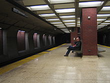 Una plataforma casi vacía de una estación subterránea de tren, con un hombre sentado en un banco