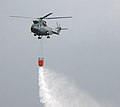 Eine Aérospatiale AS 332 wirft Löschwasser aus einem Außenlast-Löschbehälter ab.