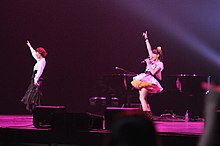 Two women performing on stage with a piano behind them