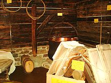 La photographie a été prise dans un musée de Beaufort-sur-Doron, hébergé dans un vieux chalet. Les murs sont en planches sombres horizontales sur un soubassement en pierre. Un chaudron en cuivre est suspendu à une potence qui peut tourner sur son axe : probablement pour la mettre et la retirer de l'âtre. Le chaudron a l'extérieur noir de suie et l'intérieur en cuivre rouge lustré. Au premier plan, un bât est chargé de deux meules encore enserrées dans leur moule pour ne pas les abîmer lors de leur transport entre le chalet d'alpage et la vallée. Aux murs sont suspendus des cercles à fromage et un tranche-caillé.