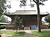 An old Chinese-style red building with large eaves with a tree in front