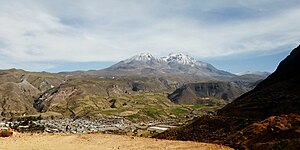 Photograph of a mountainous skyline depicting the Taapaca volcanic complex with the town of Purte in the bottom-left corner