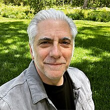 close-up of Rick Beato wearing a black t-shirt and a light grey denim jacket, squinting into camera