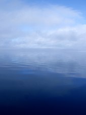 A calm, flat river surface with clouds and fog obscuring the horizon line