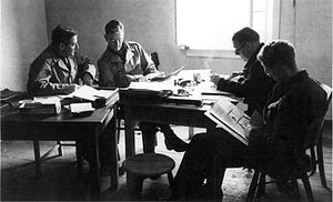 Four men in uniforms it a table reading books and documents.