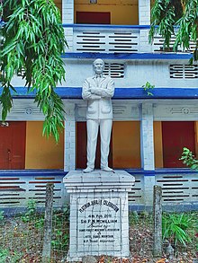 A white statue of P.N. McWilliam at McWilliam School campus. Portion of school building is visible in background.