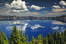 The water of Crater Lake can be seen above a forested area in the foreground.