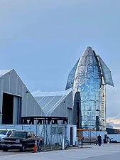 Photograph of equipment in front of white tents, with a steel nose cone at the back