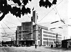 Photo d'un bâtiment important. Les rangées de fenêtres sont régulières et parfaitement alignées ; au premier plan, on devine les câbles d'un tramway.