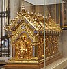 Blick auf eine Stirn- und eine Längsseite des goldenen und mit Edelsteinen verzierten Schreins, auf dem mehrere Heiligenfiguren zu sehen sind