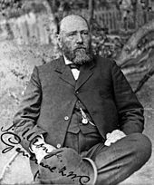 A balding man with a large beard, wearing a dark suit