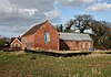 Red-brick building in a field, with a two-storey wing at right angles to a second long wing with a lower roof level. Ventilation gratings are visible in the second wing.