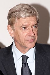 The head and shoulders of a gentleman in his 50s. He is wearing a red polo shirt underneath a blue coat, he has grey hair, and his eyes are slightly closed.