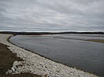 A wide river curves by a rocky shore and across a flat plain.