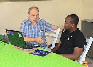 Two men sit at a laptop computer.