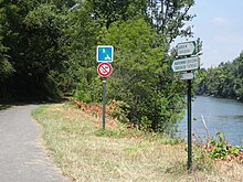 Photographie en couleurs d'une piste cyclable longeant un cours d'eau.