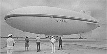 An airship standing on an airfield with several people looking at it