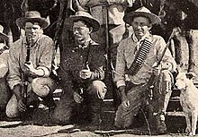 Photo taken in 1893 of three Bulawayo field scouts kneeling in front of their horses. Bob Bain on the left, Burnham in the middle, Maurice Gifford and his dog on the right. Burnham is dressed in his Arizona clothes and is holding his Winchester model 1873 .44WCF rifle