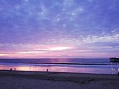 Plage lors du coucher du soleil. La couleur du ciel est violette et les nuages sont roses.