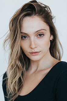 A photo of a woman with brown eyes and brown hair with blond highlights. There are two hoop earrings in her left ear.