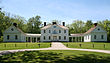 A white Palladian mansion, flanked by a wing on either side, and fronted by a green lawn in the foreground