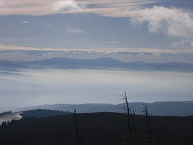 Masivul Bucegi și Masivul Piatra Craiului văzuți de pe vârful Șandru Mare (Nagy-Sándor) – 1640 m. În vale, sub nori, depresiunile Târgu Secuiesc și Sfântu Gheorghe. Este vizibilă și Crucea Eroilor de pe Muntele Caraiman.