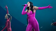 Dua Lipa performing in a pink catsuit surrounded by dancers in red outfits