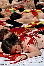 photo couleur montrant un groupe de personnes nues couchées sur le ventre simulant la mort, avec du sang et des banderilles sur le dos