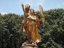 Une statue dorée d'une femme portant un rameau, devant un cheval doré également.