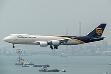 A white, black and yellow four-engined wide-body cargo jetliner about to land