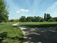 Photographie en couleurs d'une vaste pelouse naturelle avec des bosquets d'arbres.