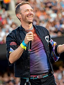 Martin on stage with his microphone, wearing a tye-die shirt and a black jacket