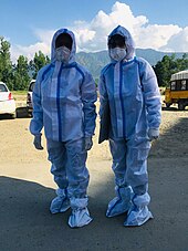 Two paramedics wearing medical PPE gowns outdoors.