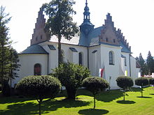 Photographie d'une église de style gothique de brique bordée par un jardin