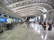 A hall with curved ceiling inside an airport. Indicators, blue screens and counters on the left side