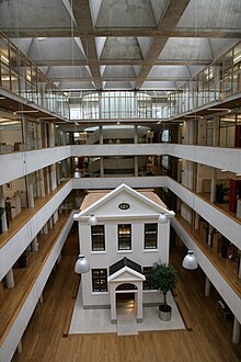 Une petite maison à un étage installée à l'intérieur de l'atrium à 5 niveaux d'un immeuble de bureaux.