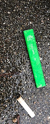 A discarded e-cigarette next to a traditional cigarette in a car park