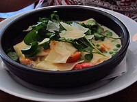 Potato and watercress soup with shaved cheese, tomato and peas