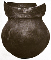 A ceramic pot with a round bottom, short neck and a rim decorated with geometric line patterns. The rim is broken in the rear.