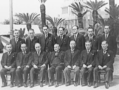 photo de groupe des ministres. Une douzaine d'hommes en uniformes sont rassemblés en extérieur sur deux rangs. Les hommes du premier rang sont debout, les hommes du second rang sont debout.