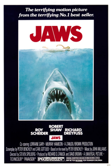 Movie poster shows a woman in the ocean swimming to the right. Below her is a large shark, and only its head and open mouth with teeth can be seen. Within the image is the film's title and above it in a surrounding black background is the phrase "The most terrifying motion picture from the terrifying No. 1 best seller." The bottom of the image details the starring actors and lists credits and the MPAA rating.