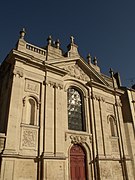 Bâtiment en pierre avec une porte rouge et un vitrail au-dessus.