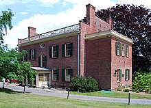 The rear of a classic, red-brick building with beige trim is shown beyond a driveway.