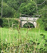 Photo d'un pont en pierre qui semble posé au milieu d'un champ bien vert.