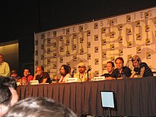 A long table with a group of white men sitting behind it, each with a microphone in front of them